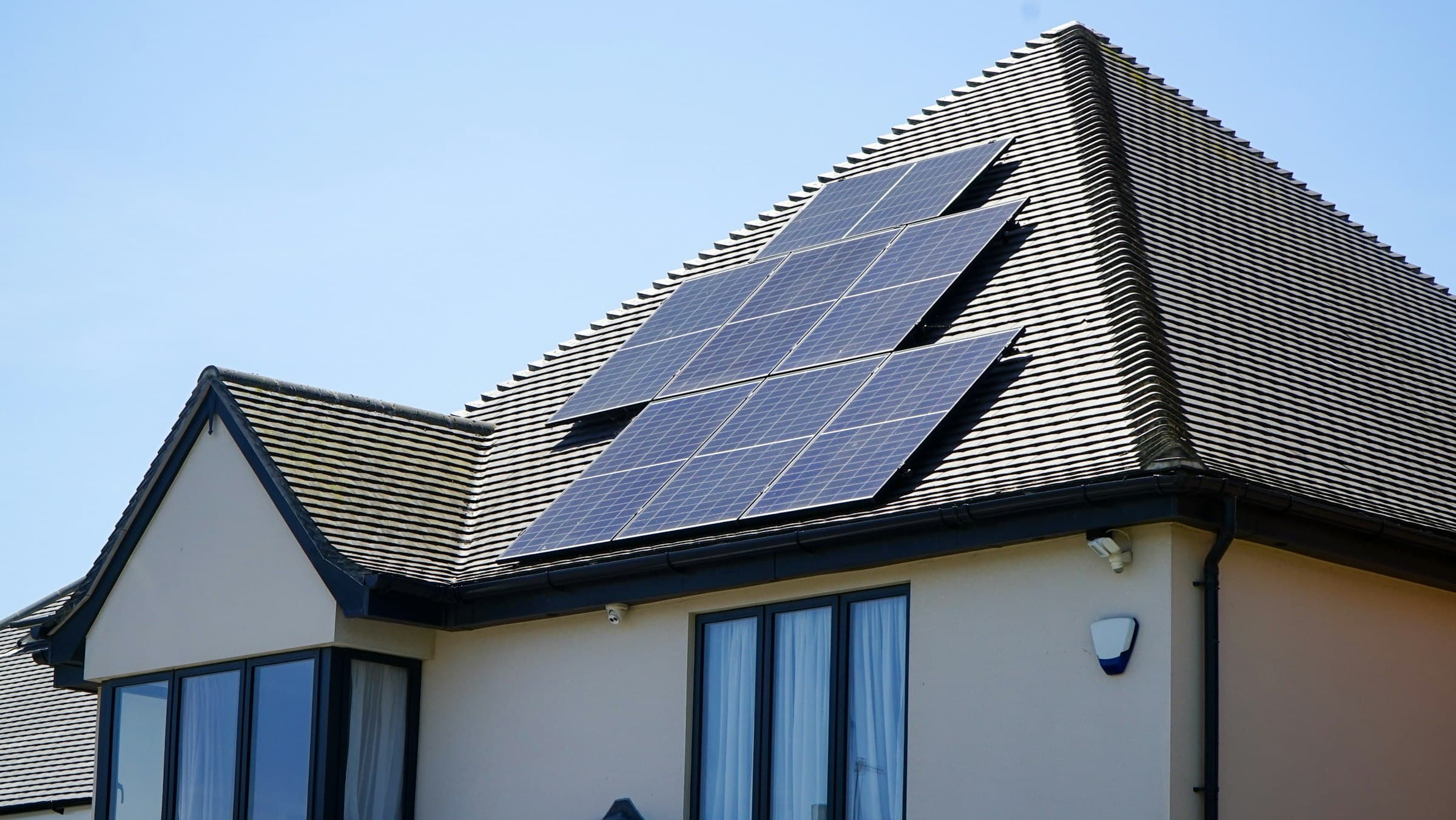 Two-storey home with solar panels on a dark tiled roof under a clear blue sky